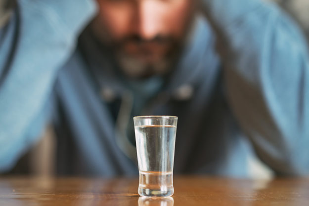a man looks at a shot glass and considers the effects of alcohol and anxiety