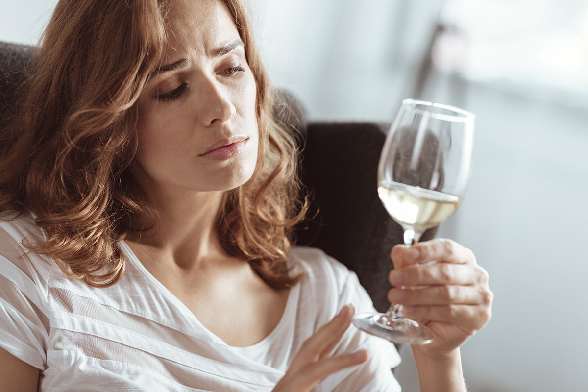 a woman holds a glass of wine and thinks about the signs of an alcohol addiction