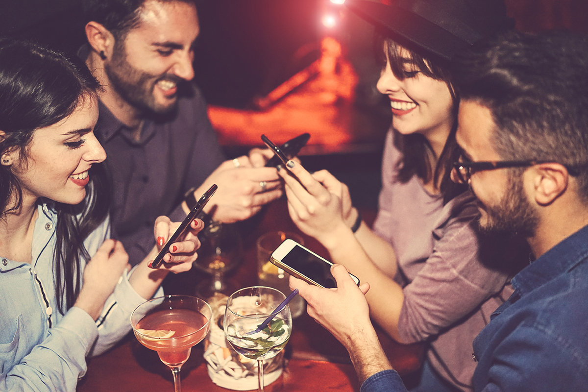 a group of people use their phones to research drinking and social media while they're out on the town